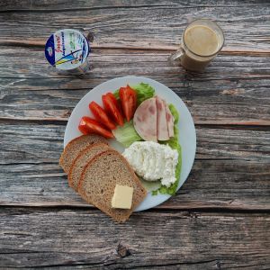 Zdjęcie przedstawia Dietę z ograniczeniem łatwoprzyswajalnych węglowodan&oacute;w: Kawa zbożowa z mlekiem Jogurt naturalny Chleb Graham Masło extra Szynka Drobiowa Pomidor Sałata lodowa Serek a'la homogenizowany